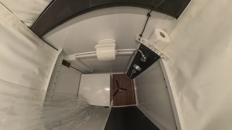 Inside the High Country flatbed pop-up wet bath showing the cassette toilet, shower head, and wood-look floor