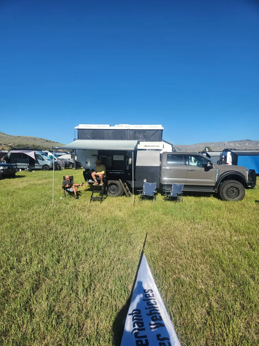Two people relaxing under the awning of an OEV Hudson Bay pop-up camper at the OEV booth during The Big Thing 2026