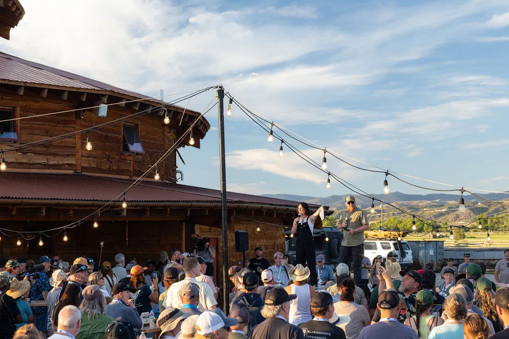 Event hosts addressing a crowd gathered under string lights by the timber pavilion at The Big Thing 2026, XOVERLAND Ranch