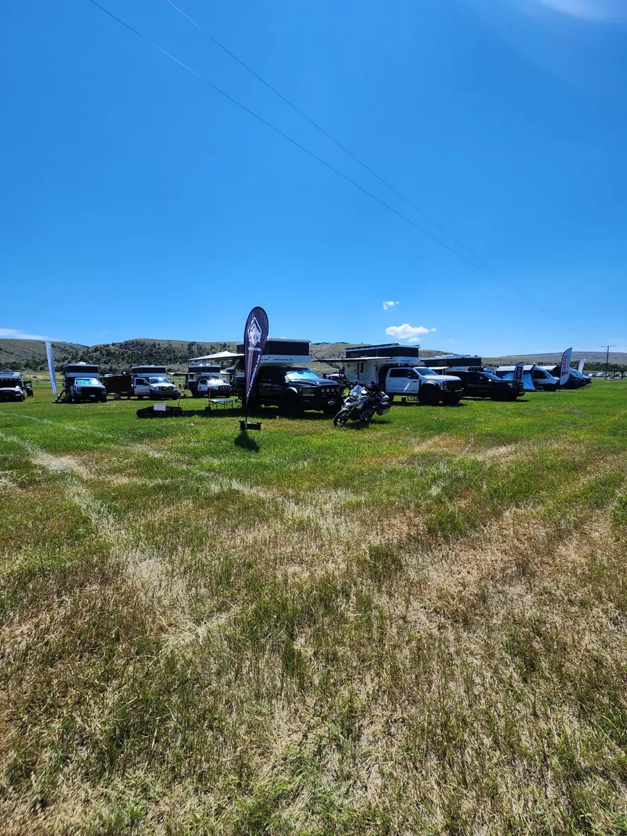 Overland campers, trucks, and vendor banners spread across a grassy field at The Big Thing 2026 overland event in Three Forks, Montana