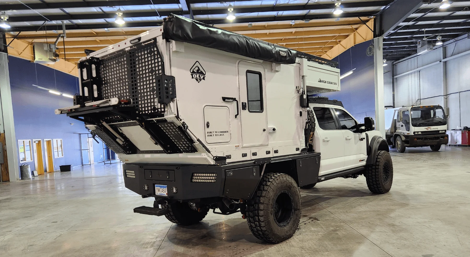 High Country flatbed pop-up rear three-quarter view showing the angled rear kick-out with molle panels and a fold-down rack